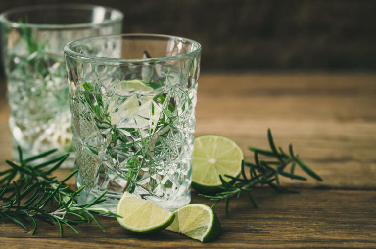 Glasses with a refreshing lime rosemary drink, lime halves and rosemary branches on old wood
