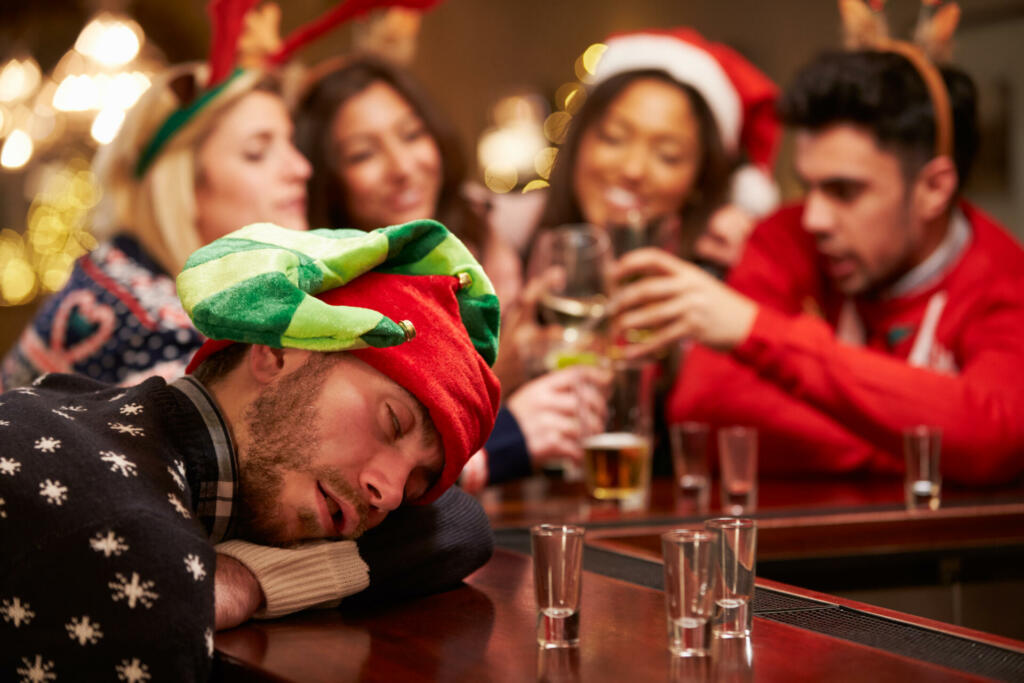 Man Passed Out On Bar During Christmas Drinks With Friends, Wearing Christmas Hats