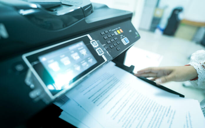 Office worker print paper on multifunction laser printer. Copy, print, scan, and fax machine in office. Modern print technology.  Photocopy machine. Document and paper work. Scanner. Secretary work.