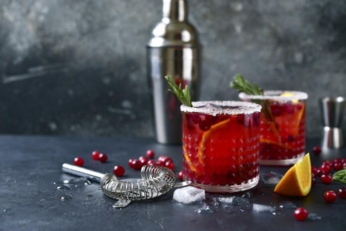 Red christmas cocktail with cranberries and oranges in a glasses on a dark slate, stone or concrete background