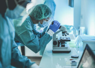 Največja znanstvena odkritja 2022 Scentist people working inside laboratory with microscope and laptop while wearing hazmat suit and face masks - Focus on the young woman with microscope