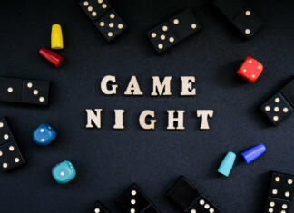 5 idej za novoletne igre, ko ti zmanjka časa za pripravo Text GAME NIGHT spelled out in wooden letter. Surrounded by dice, dominoes other game pieces on black background. Table games. Stay home activity for kids family.