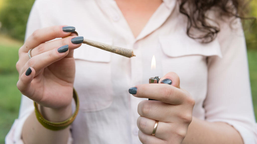 The young person smoking medical marijuana joint outdoors. The young woman smoke cannabis blunt, close-up. Cannabis is a concept of herbal alternative medicine.