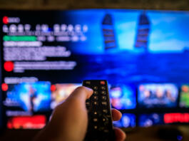 TV remote control in the foreground, Video on demand screen in the blurry background, streaming