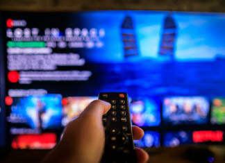 Zakaj so pretočne platforme vse dražje? TV remote control in the foreground, Video on demand screen in the blurry background, streaming