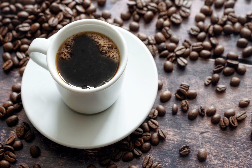 White cup with strong black coffee on a rustic wooden table with some beans, copy space, selected focus, narrow depth of field