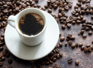 Preden se kava ohladi pripoveduje o krhkosti in lepoti človeških življenj White cup with strong black coffee on a rustic wooden table with some beans, copy space, selected focus, narrow depth of field