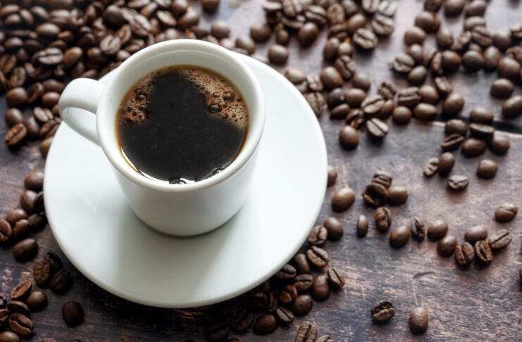 White cup with strong black coffee on a rustic wooden table with some beans, copy space, selected focus, narrow depth of field