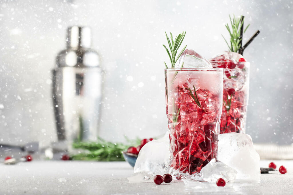 Winter alcoholic cocktail with red cranberry berries, liquor, gin, rosemary and vodka for Christmas or New Year celebration. Holiday table setting