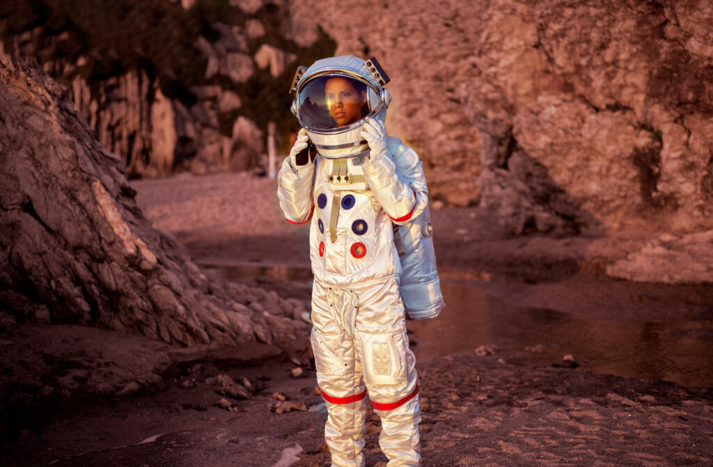 Astronavtka v skafandru stoji v kamniti rdečkasti pokrajini