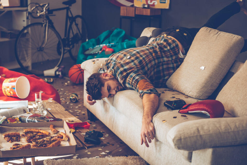 Young handsome man passed out on sofa in messy room after party