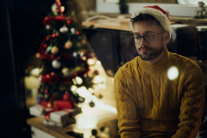 Young pensive man feeling lonely while spending New Year's eve alone at home.