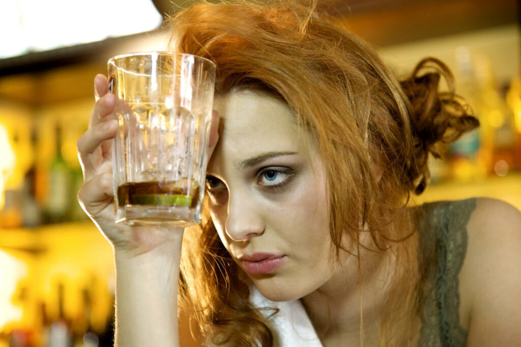 Young woman with a hangover holding her almost empty cocktail glass