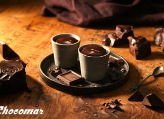 Najboljše začimbe za vročo čokolado Skodelici vroče čokolada na pladnju, okoli so kosi temne čokolade