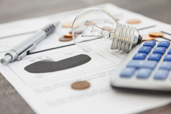 A light bulb, a pen, a calculator and some copper euro cent coins lie on top of an electricity bill.