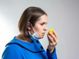 Ženska s kirurško masko pred nosom drži limono in jo vonja