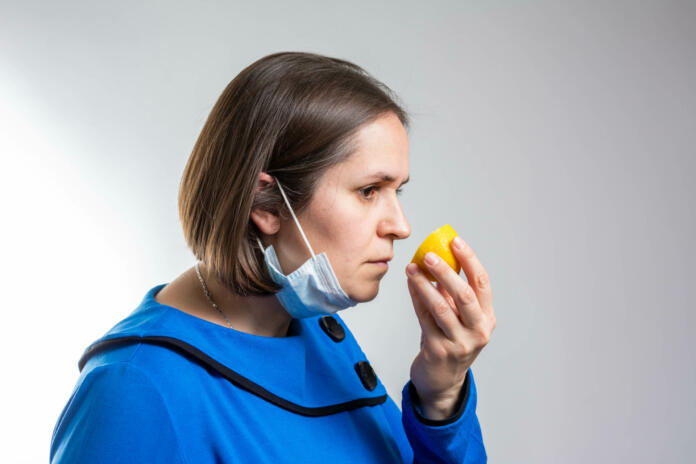 Ženska s kirurško masko pred nosom drži limono in jo vonja