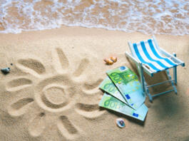 Deckchair with euro bills on a beach with a sun drawn on the sand. Travel money savings concept