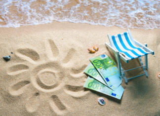 Slovenija z milijoni v turizem Deckchair with euro bills on a beach with a sun drawn on the sand. Travel money savings concept