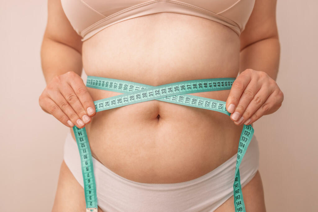 Fat woman, fat belly, plump, obese woman holding excess belly fat with measuring tape on beige background, female diet lifestyle concept