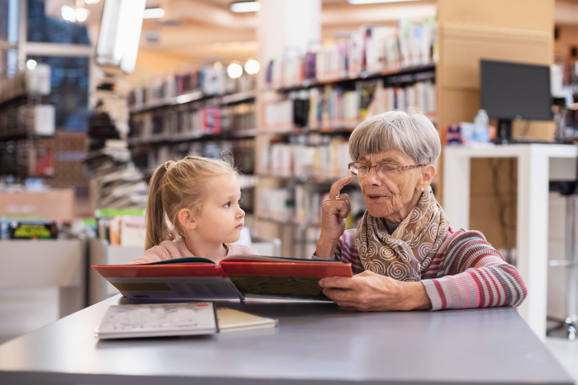 Grandmother reads a book to her granddaughter at the library