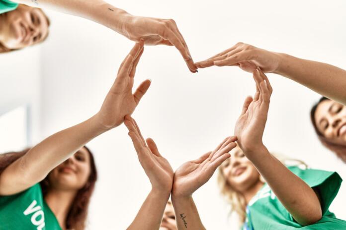 Group of young volunteers woman smiling happy make heart symbol with hands together at charity center.