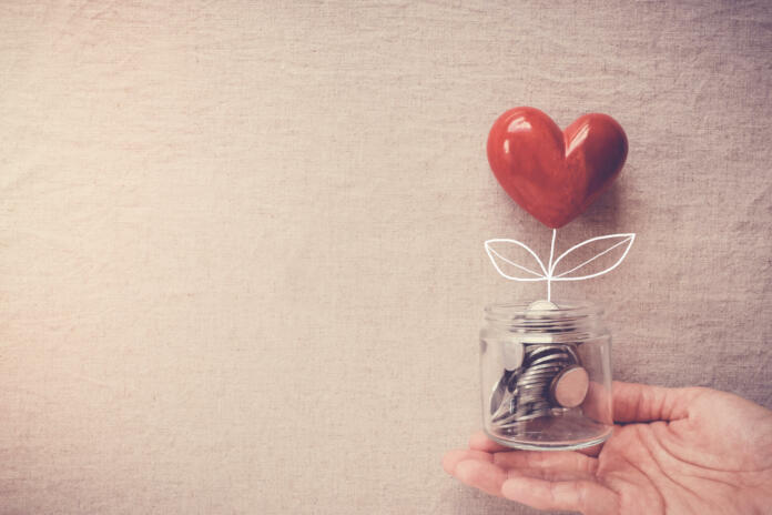 Hand holding a jar of heart tree growing on money coins, social responsibility and donation concept