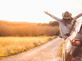 Happy girl celebrating success at sunset. The girl is wearing a hat and her arms are outstretched.