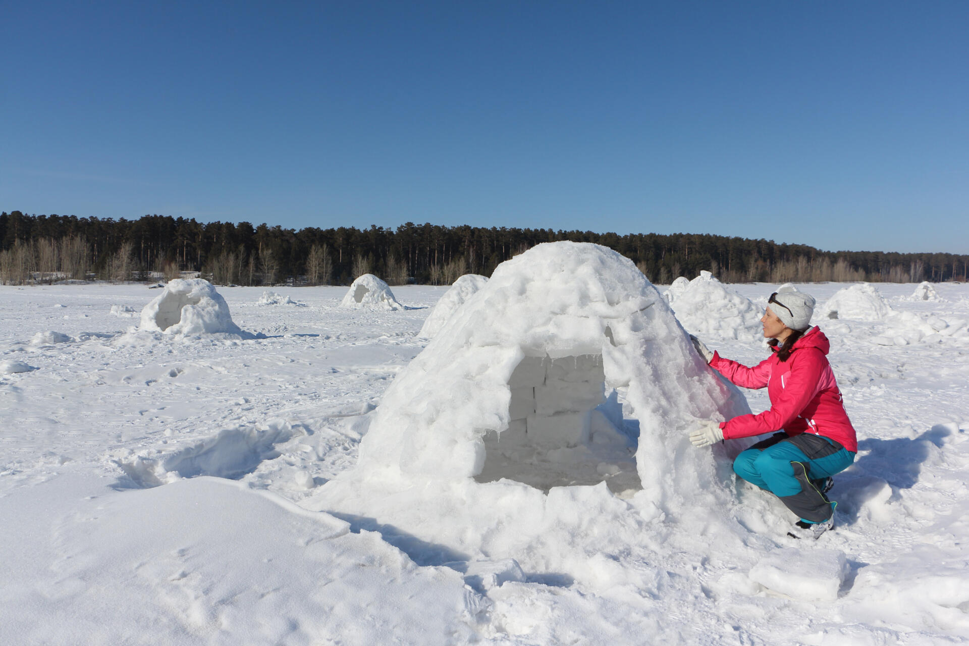 Happy woman a red jacket building an igloo on a snow glade in the winter