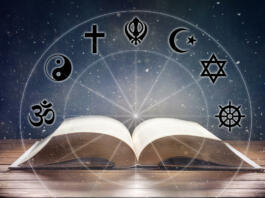 Open book on wooden table with religious symbols and universe background. Concept of the study of religions. Front view.