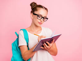 Portrait of concentrated reader student girl writes in notebook isolated on vivid pink background with copy space for text