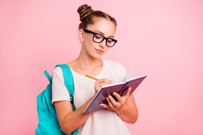 Portrait of concentrated reader student girl writes in notebook isolated on vivid pink background with copy space for text