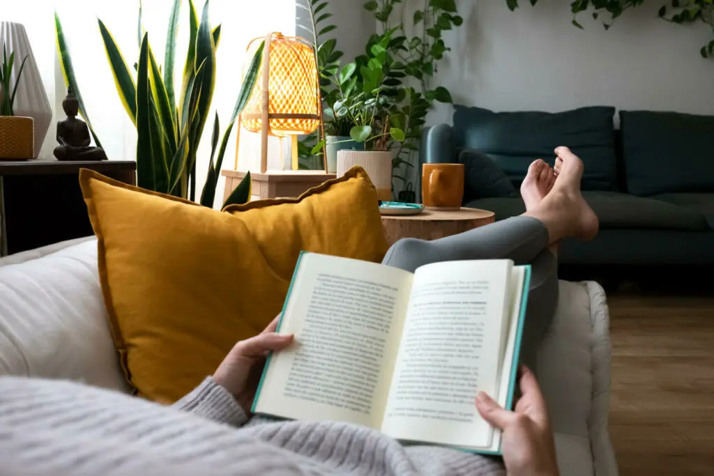 POV of young woman relaxing at home reading a book lying on sofa. Lifesyle concept.