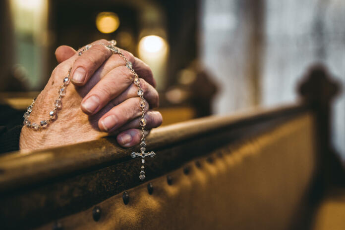 Praying senior hands with rosary in church bench