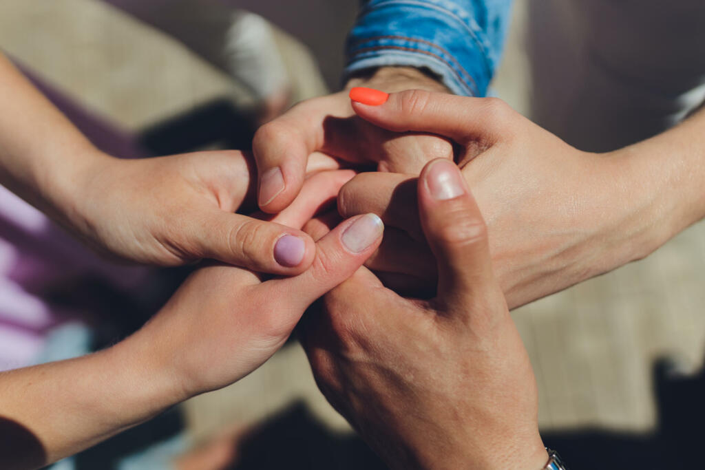 two man and three women holding hands on a table implying a polyamory relationship or love triangle