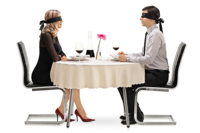 Young man and woman on a blind date seated at a restaurant table isolated on white background