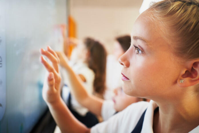 Young student girls interacting with digital blackboard