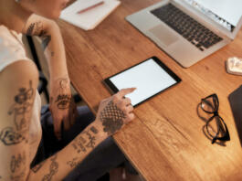 Young tattooed woman with short haircut using digital tablet while sitting at her workplace. Business woman at work. Cropped view. Workplace. Business concept