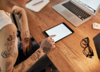 Kaj je e-tatu? Young tattooed woman with short haircut using digital tablet while sitting at her workplace. Business woman at work. Cropped view. Workplace. Business concept