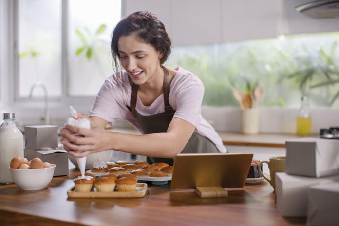 Young woman pouring cream on the cupcake in the kitchen