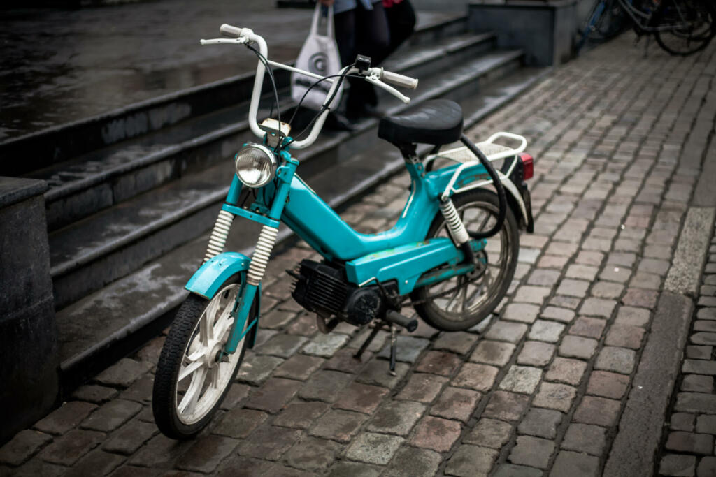 A retro moped / motorbike bike parked up on a cobblestone pavement