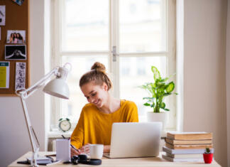 Enak ali isti? To je zdaj vprašanje! A young happy college female student sitting at the table at home, studying.