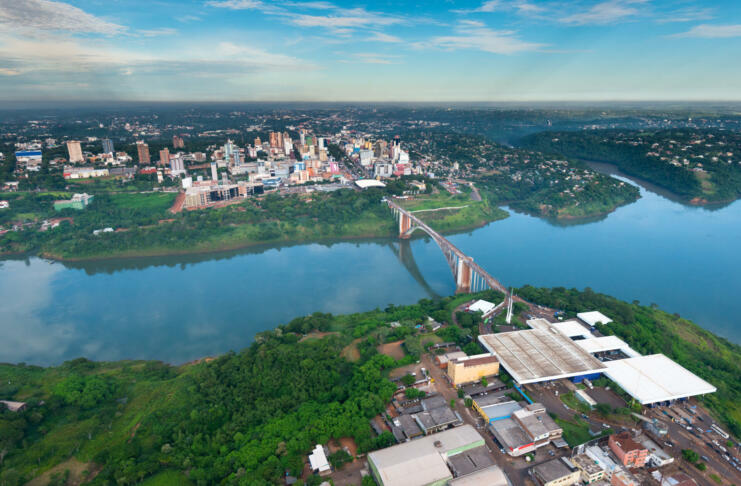 Aerial view of the Paraguayan city of Ciudad del Este and Friendship Bridge, connecting Paraguay and Brazil through the border over the Parana River, with Brazilian customs and immigrations facilities in the foreground.