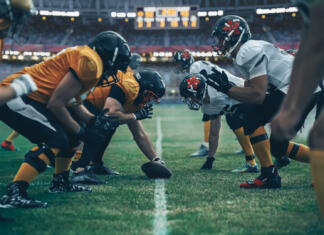 Ponavljajoči se udarci z glavo povzročijo CTE American Football Championship. Teams Ready: Professional Players, Aggressive Face-off, Ready for Pushing, Tackling. Competition Full of Brutal Energy, Power. Stadium Shot with Dramatic Light