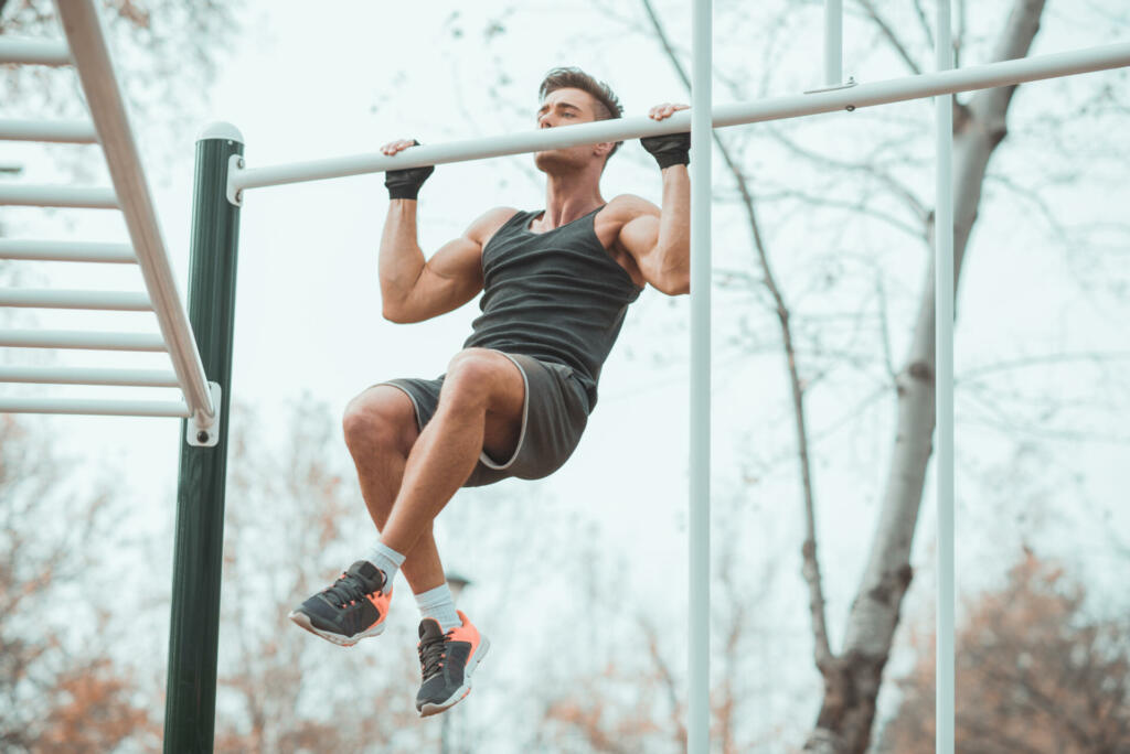 An attractive young man with sports gloves is seen doing chin-ups.