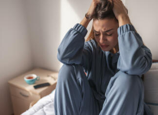 Si pod stresom? Imamo rešitve! Anxious young woman wearing pajamas, sitting on bed in the morning, holding head in hands, crying