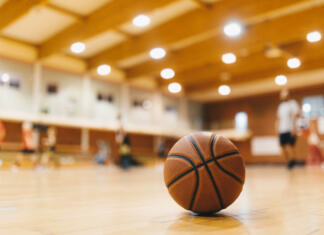 Najboljši dokumentarni filmi o košarki Basketball Training Game Background. Basketball on Wooden Court Floor Close Up with Blurred Players Playing Basketball Game in the Background