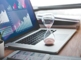 Business concepts with businessman holding hourglass with graph chart on computer laptop.For investment analysis,Waiting to sucess ideas