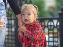 Caucasian little girl of 2 years with scared face holding hand of mother in summertime outdoors