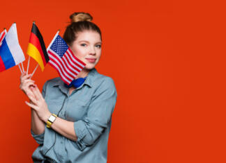 Oddaj vlogo za štipendijo za študij v tujini Caucasian student girl holds set small flags. Study abroad concept. International student exchange program. Female student recommending foreign language studying school. Copy Space